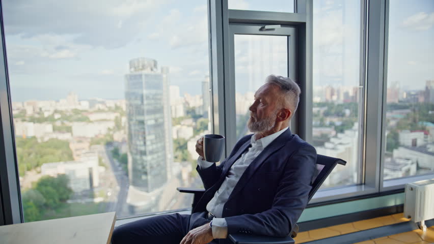Successful entrepreneur holding cup coffee sitting comfortable office chair. Relaxed senior businessman sipping beverage looking panoramic window. Elegant manager making work break enjoying cityscape.