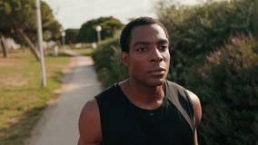 A young African American man jogs in a park on a sunny summer day. He is focused on his workout and enjoying the outdoors. - Powered by Shutterstock - Get 15% off with code: PIKWIZARD15