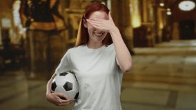 Woman standing in a church holding a soccer ball, smiling with hand covering eyes, suggesting joy and diversion within a sacred setting. - Powered by Shutterstock - Get 15% off with code: PIKWIZARD15