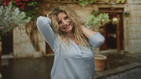 Woman touching chin with hand and flipping hair while smiling, standing in front of an old stone building with potted plants; confidence. - Powered by Shutterstock - Get 15% off with code: PIKWIZARD15