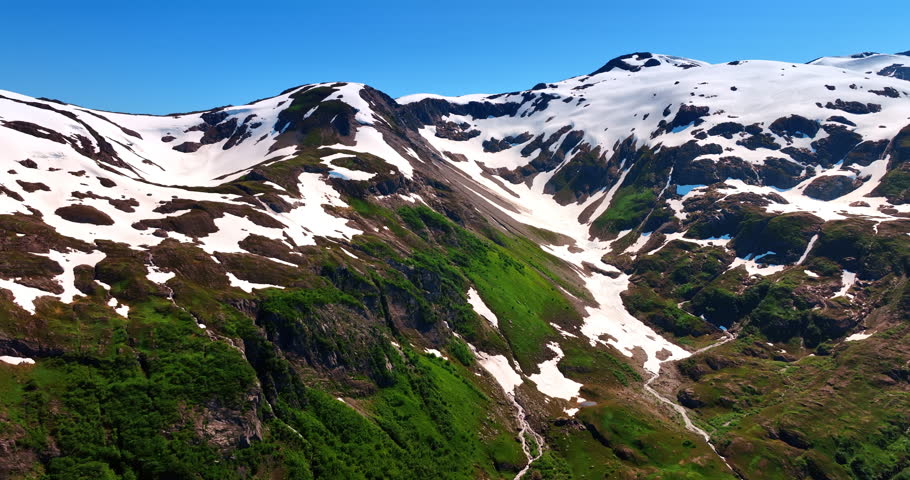 Distancing from the mountain top covered with some snow. Drone footage over the gorgeous rocks on sunny day. Alaska nature.