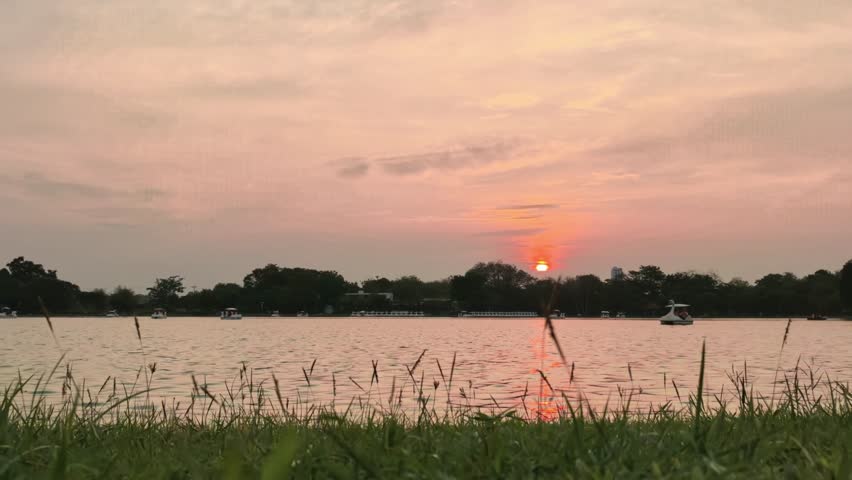 Serene Sunset Over Calm Lake with Boats and Grass