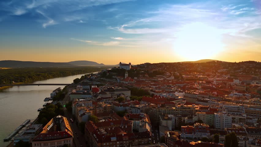 Setting sun lights the orange roofs of the historical part of Bratislava, Slovakia. Bratislava Castle at backdrop. Footage near the Danube.
