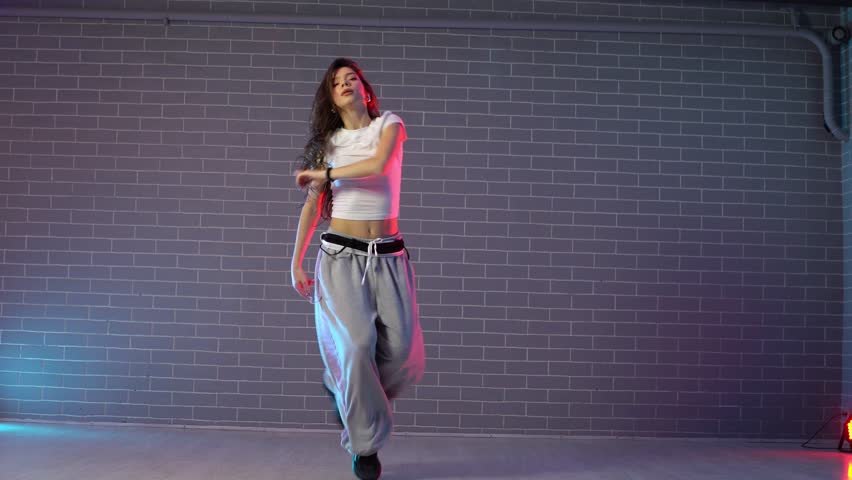 young crazy girl dancing hip hop against wall background in neon lighting, female choreographer moving to music and performing jazz funk in dance studio