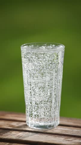 glass of fresh sparkling mineral water on green summer garden background