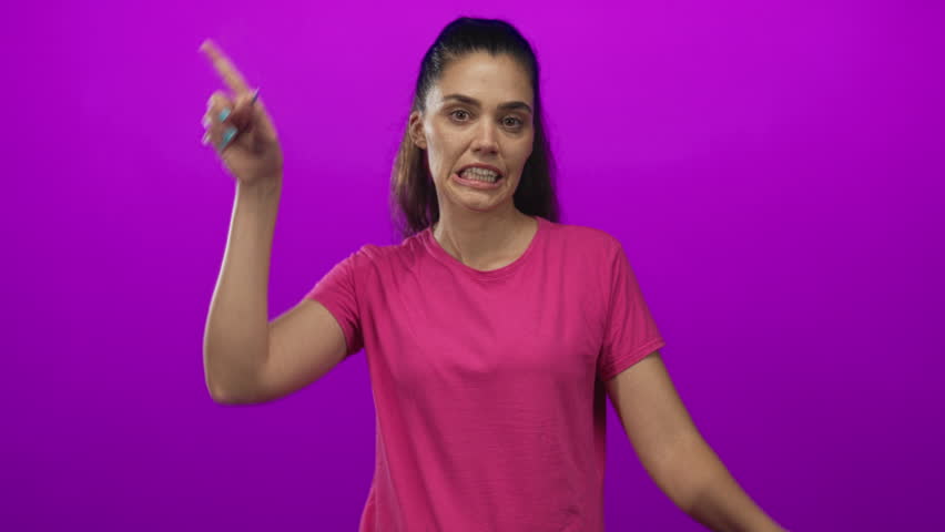 Woman making finger horns on head in studio with bright magenta backdrop, visible hands and pink tee; playful mischief.