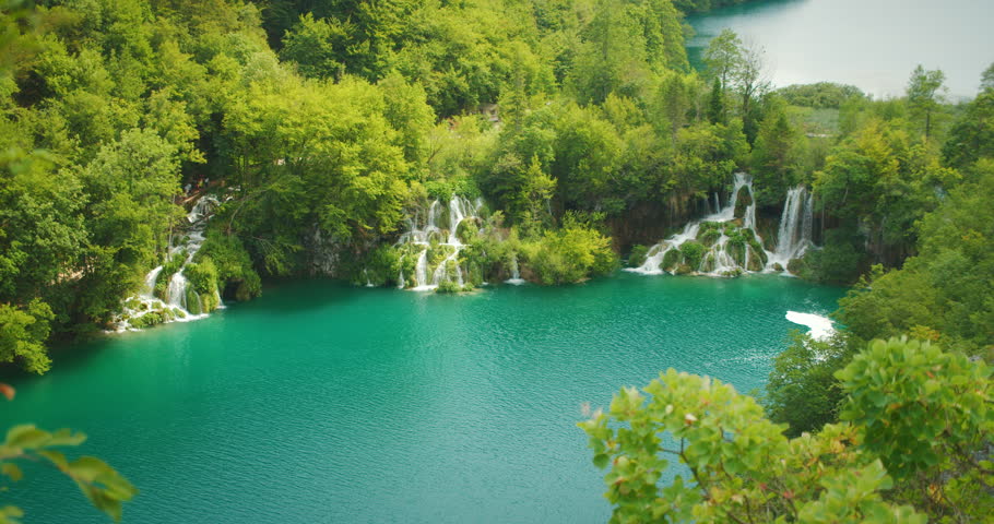 Waterfalls feed into a vivid turquoise lake by forest at Plitvice Lakes Park Croatia
