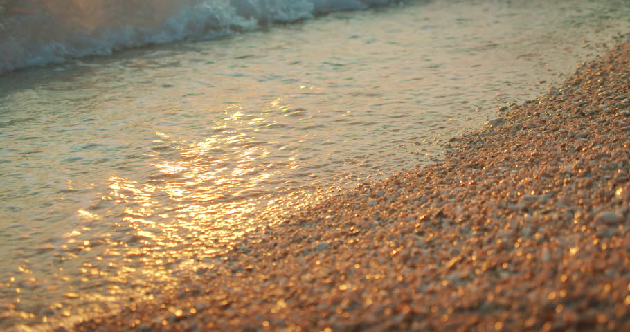 Barefoot woman runs along pebble beach at golden sunset with soft sea waves