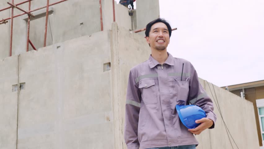 Asian male worker, plumber working outdoors construction site in a hot and humid residential building taking break to drink water to refresh himself.
