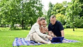 Happy family couple sitting in the park on the grass and looking at the laptop screen with their son.. family couple with child watching a movie sitting on the grass. Happy family concept - Powered by Shutterstock - Get 15% off with code: PIKWIZARD15