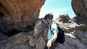 Senior cyclist wearing helmet and backpack hikes in volcanic mountain landscape in the Canary Islands, reaching a rocky summit with his electric bike in slow motion - Powered by Shutterstock - Get 15% off with code: PIKWIZARD15