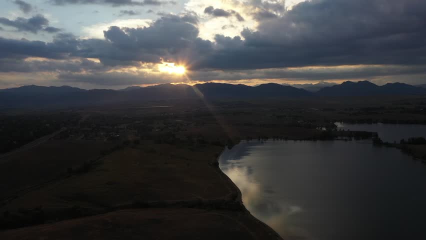 Panning Drone Shot of Sun Peeking Through Clouds at Sunset Over Colorado Mountains and a Lake