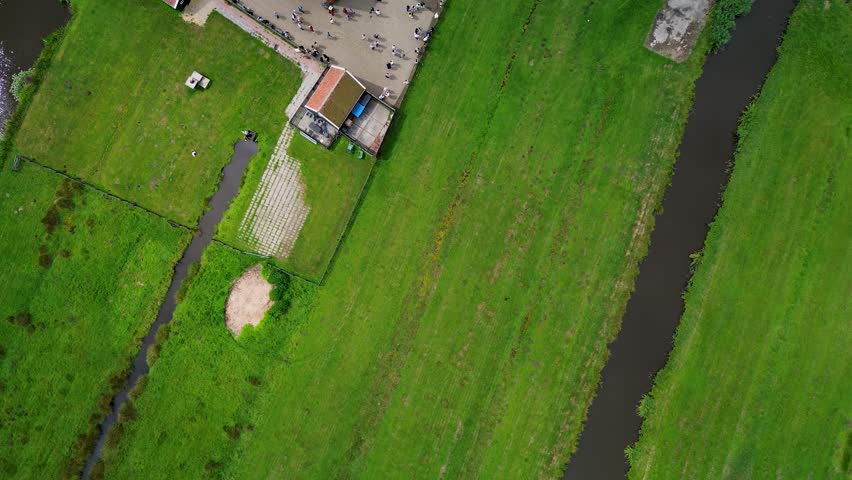 Amsterdam, North Holland, Netherlands - 09.06.2025: Aerial view of a Dutch harbor with sailboats, traditional black wooden houses with red roofs, and a waterfront promenade in a scenic village.