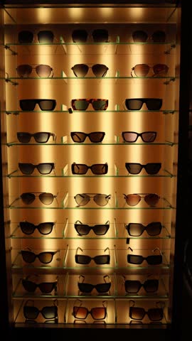 Vertical screen sunglasses collection displayed on illuminated glass shelves in luxury store symbolizing fashion lifestyle elegance shopping choices and modern urban accessory trends