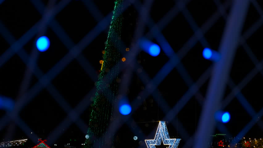 Christmas tree with red star seen through blue lights blur. Glimmering christmas tree adorned with vibrant red star, softly blurred through sparkling blue illumination against dark nocturnal backdrop