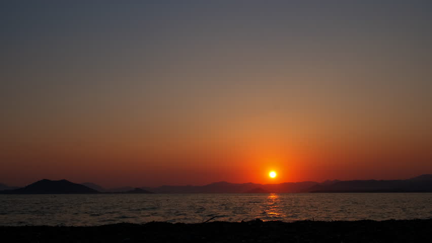 Orange sun over lonely dusk sea. A view of calm orange horizon over the abandoned lake during summer time