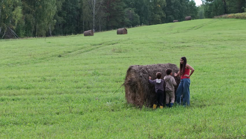 Family pushing hay bale in field