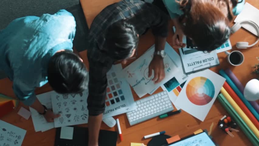Top down aerial view of project manager looking at screen while designer writing idea. Smart business team explain idea of logo design while designer choose theme while looking at palette. Symposium.