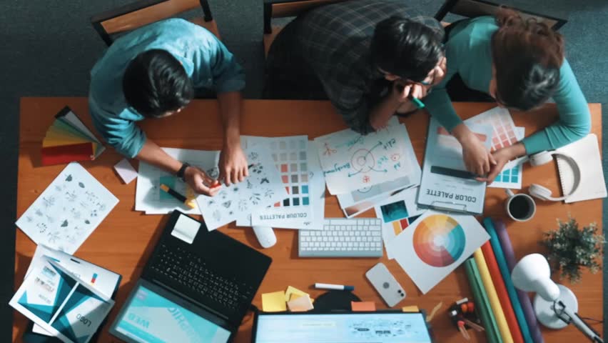 Top down aerial view of project manager looking at screen while designer writing idea. Smart business team explain idea of logo design while designer choose theme while looking at palette. Symposium.