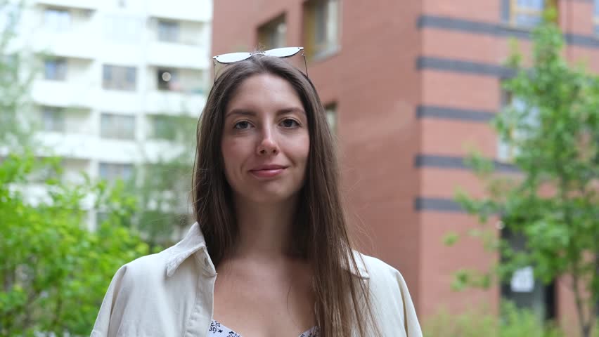 Cute cheerful charming girl poses for camera in summer on city street, hands and fingers showing V sign