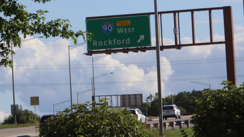 4K video of a green road sign above a highway showing Intrestate 90 heading west towards Rockford, Illinois. 