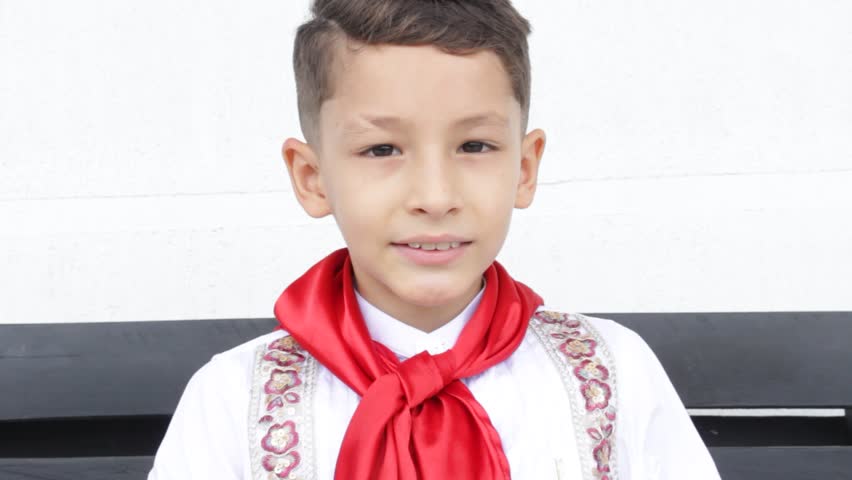 A Latino boy wearing a suit smiling and looking at the camera is placing a sombrero on his head against a white background in Neiva, Huila, Colombia. A concept of childhood and Colombian culture