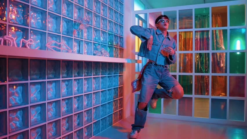 Asian performer with sun glasses moving freestyle dance while looking at camera at nightclub. Happy street dancer dancing and show footstep with colorful bright neon light or led light. Regalement.