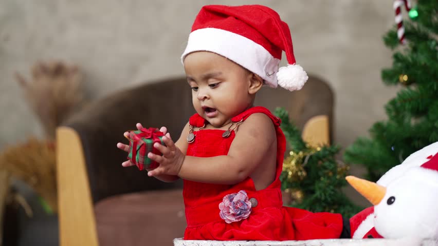 African baby toddler in santa costume standing in the box playing with Christmas stuff, winter season holiday