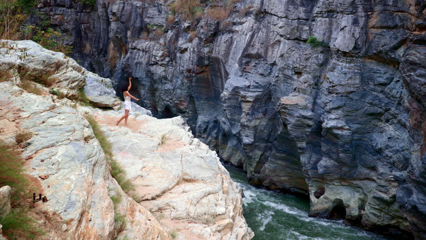 A Brave Individual Standing on the Edge of a Rugged Cliff Overlooking a Flowing River, Showcasing Fearlessness and Natures Beauty in a Dramatic Landscape