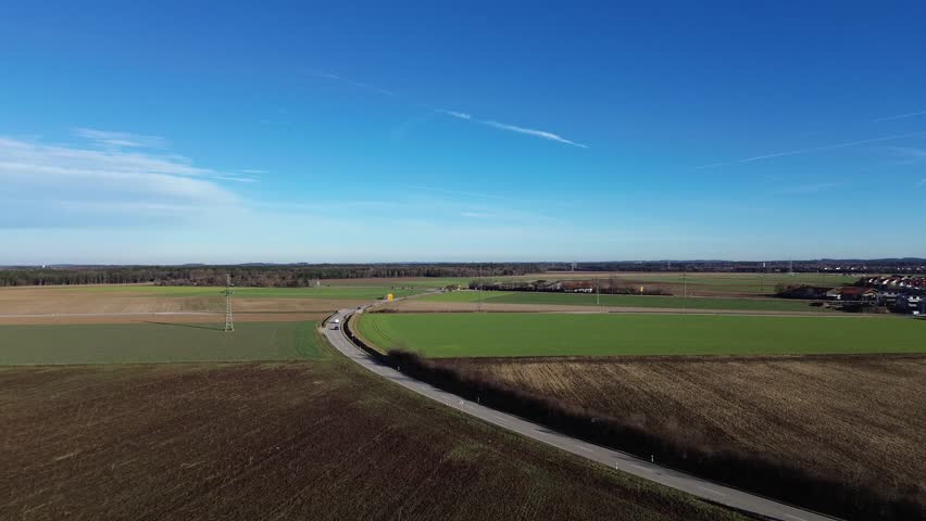 Aerial view of curving rural road through patchwork farmland near Lower Saxony, Germany. Clear blue sky and open fields evoke tranquility and order in this structured countryside scene.