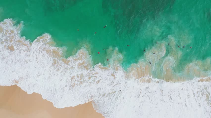 Drone video of North Shore, Oahu captures surfers riding turquoise waves, overhead. The beach break scene with dynamic splashes and golden sands unfolds under natural daylight.