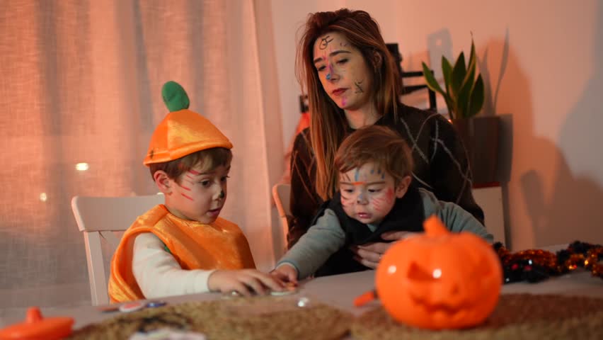 Mother and children enjoying halloween, wearing costumes and makeup, playing at a table decorated with pumpkins
