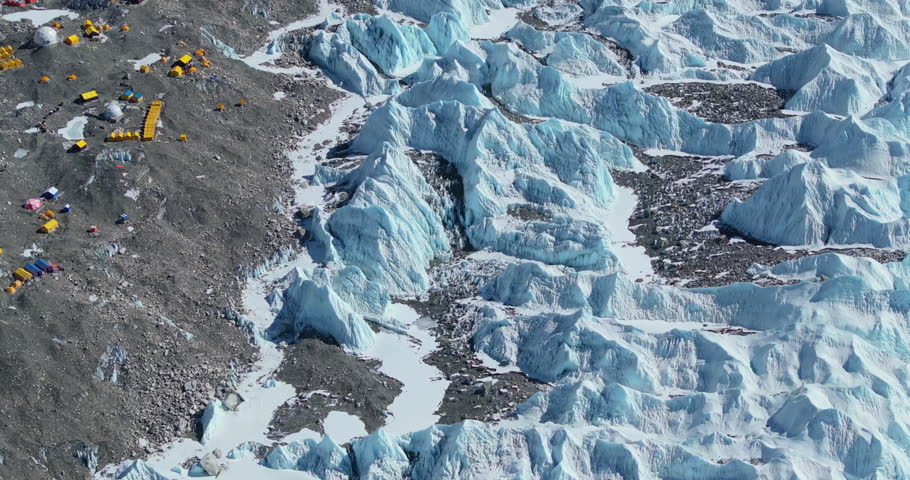Close-up drone shot of Everest Base Camp and Khumbu Glacier, Nepal in dense snow, melting ice, Sagarmatha peaks, high-altitude tents, layered Himalayan mountains under sunny skies, adventurous travel