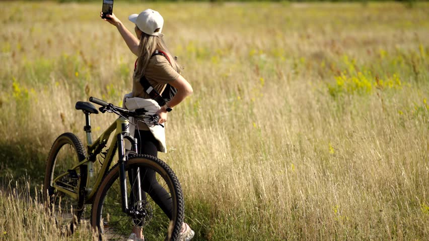 Takes Selfie With Mountain Bike. Female Cyclist Capturing Moment. Active Lifestyle And Social Media. Solo Biker In Sunny Field. Outdoor Recreation. Adventure And Leisure. Modern Digital Nomad