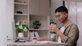 Asian man smiles and drinks coffee at his home office desk, placing the cup down before beginning work in the morning. Slow motion 4K video ideal for lifestyle, remote work, and productivity content. - Powered by Shutterstock - Get 15% off with code: PIKWIZARD15