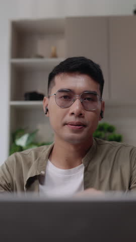 Vertical video of an Asian man standing up from desk and leaning toward the camera as if searching for something. Captured in modern home office, ideal for lifestyle, business, or short-form content.