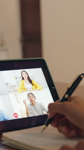 Vertical Screen : Asia businesswoman using digital tablet talk to colleague about plan by video call brainstorm online meeting while remotely work from home at kitchen. Social distancing, quarantine.