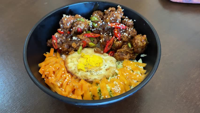 Delicious black pepper chicken rice bowl served with fried egg, fresh vegetables, and carrot strips with mayonnaise, garnished with sesame seeds and chili slices