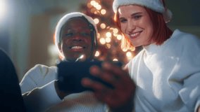 Happy people using mobile gadgets in Christmas night, laughing man and woman. Portrait of black guy and caucasian lady smiling when chatting online with friends or family, video call by mobile phone - Powered by Shutterstock - Get 15% off with code: PIKWIZARD15