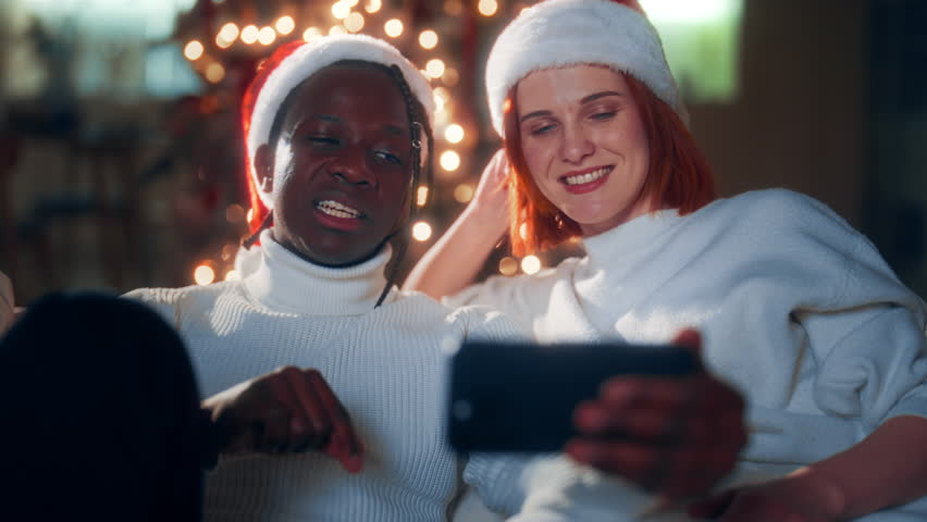 Portrait of man and woman chatting by video call in smartphone in Christmas. Modern technology of communication, biracial loving couple celebrating Xmas, smiling faces of black guy and caucasian lady - Powered by Shutterstock - Get 15% off with code: PIKWIZARD15
