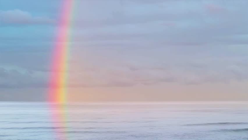 Multicolored rainbow in rainy sky over sea. Panorama with clouds and ocean.
