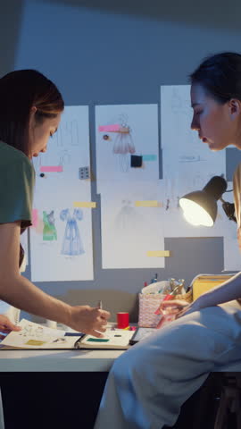 Vertical Screen : Two Asia cheerful lady fashion designer teamwork with casual overtime work discuss meeting on table share idea create dress collection at night. Lady tailor partner start up business