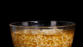 A pair of chopsticks stirs steaming instant noodles in a clear glass bowl against a black background, with even studio lighting and minimal camera movement - Powered by Shutterstock - Get 15% off with code: PIKWIZARD15