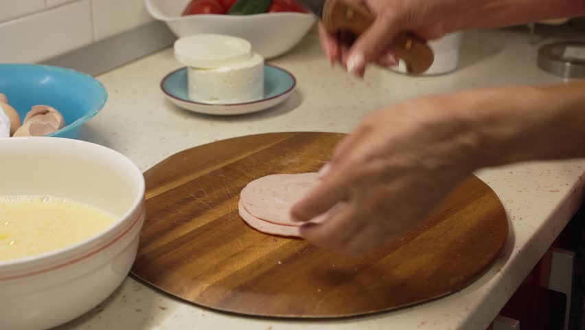 Woman chopping pork ham on a wooden cutting board to add into an omelette mixture in a bowl