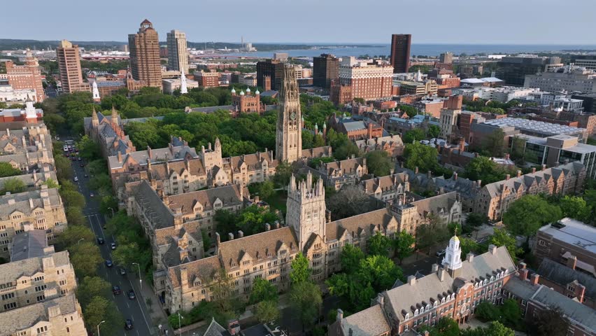 Harkness Tower at Yale old campus university of New Haven. American City in Connecticut at sunrise. Summer day with green trees. Connecticut Financial Center In background. Aerial approaching shot.