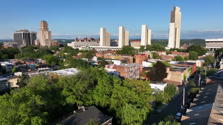 Row homes and two-story houses in red brick style in front of downtown skyline. Sunny day with blue sky in Albany, New York. Aerial wide shot. New York State capitol and Empire State plaza in back.