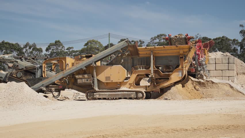 A mobile sand crusher processes raw material at a quarry site. The tracked machine crushes and screens sand for use in construction and cement production.