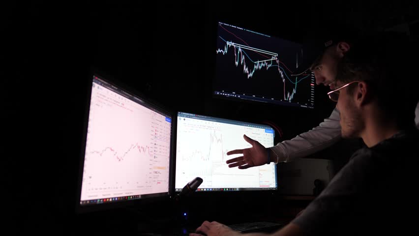 Two young traders discussing crypto trading charts growth using pc computer. Male brokers analyzing financial risks and investment profit forecast at night. Concept of stock market and data analysis