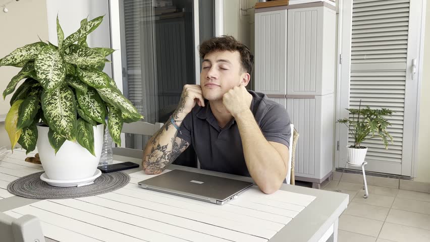 Young smiling boy while using his computer sitting in outdoor terrace. A laptop is open in front of him, suggesting he might be working or studying remotely