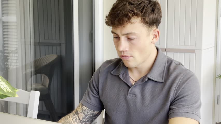Young smiling boy while using his computer sitting in outdoor terrace. A laptop is open in front of him, suggesting he might be working or studying remotely